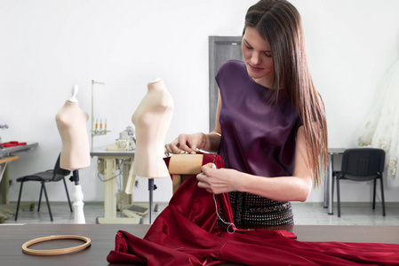 年轻漂亮的裁缝在工作室或工作室缝制红色连衣裙
