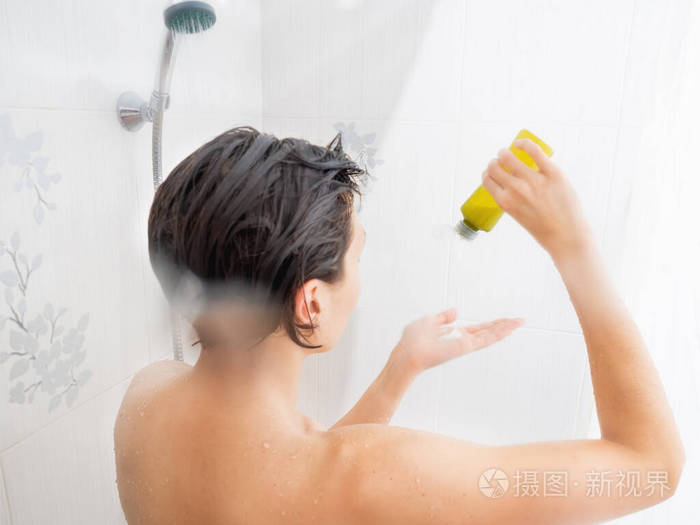 裸体短发女人洗澡女人从绿色瓶子里挤出洗发水白色浴室