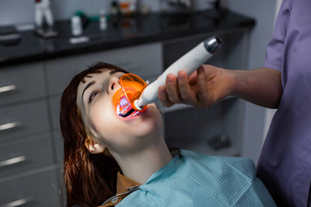 在牙医诊所接受牙科治疗的年轻女性患者。牙科医生用紫外线灯对患者进行牙科治疗