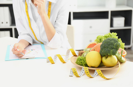 Nutritionist at desk with fruits, vegetables and measuring tape 