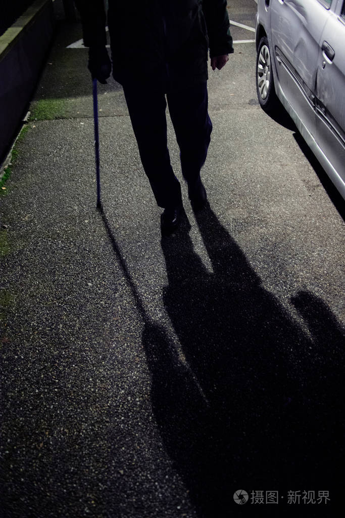 较低高度的老年人轮廓行走在法国街道夜间使用手杖保持平衡与蓝色伸缩