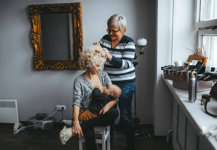 理发师,发型师为年轻的母亲做卷发,她正在给刚出生的孩子喂奶照片