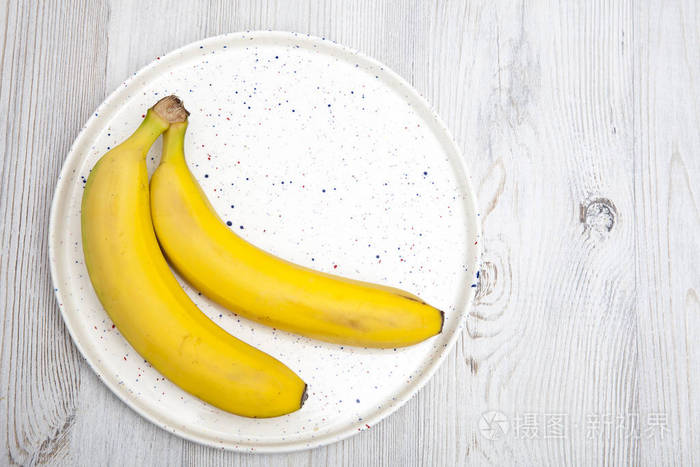 两个香蕉放在一张灰色的木桌上的白色盘子里