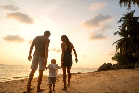 夕阳下，一家人快乐地沿着热带海滩散步