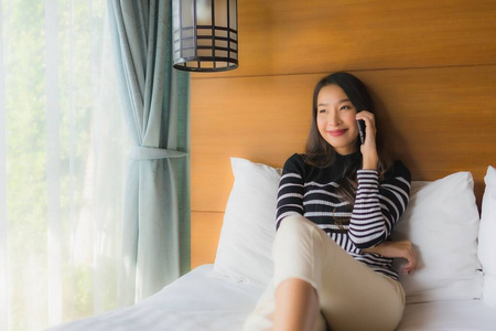 年轻的亚洲女人在床上用智能手机拍照