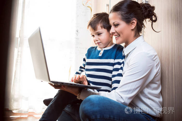 妈妈和儿子坐在地板上看着笔记本电脑与某人视频通话