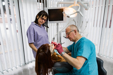 现代牙科诊所的牙医团队为年轻女性患者进行牙齿治疗。现代牙科诊所高级男牙医及其助手