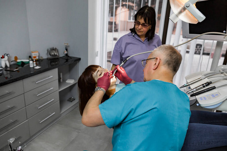 女患者在牙科钻牙治疗期间张口。专业牙科团队男女为年轻女性患者做治疗
