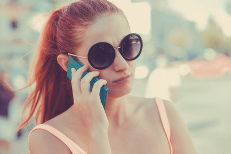 Serious red head woman talking at phone outdoors city 