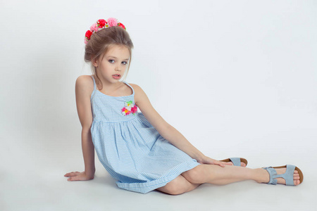 小女孩在摄影棚里摆姿势,坐在地板上,头上戴着红粉色的花头巾,浅蓝色