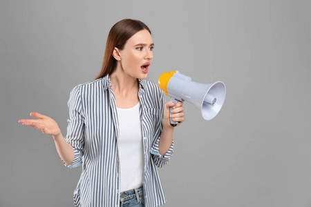 Emotional young woman with megaphone on light grey background