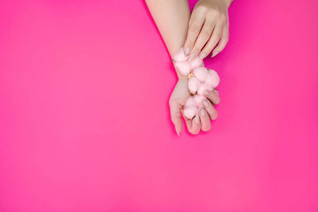 在明亮的背景上，用柔和的粉红色棉质，为美丽的女性修指甲。