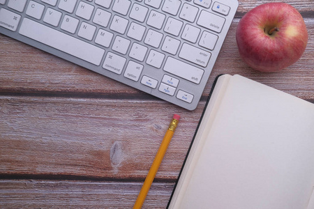 top view of keyboard, pencil, notepad and apple on table 