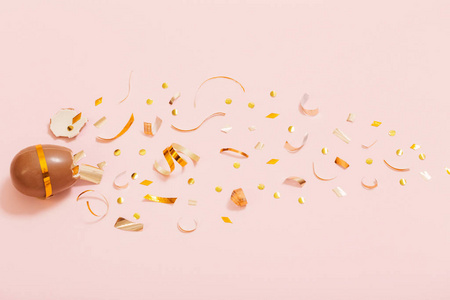 Easter chocolate egg with golden confetti on pink background 