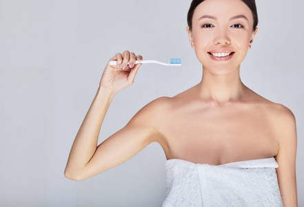 一位年轻的亚洲妇女洗澡后穿着白毛巾刷牙。