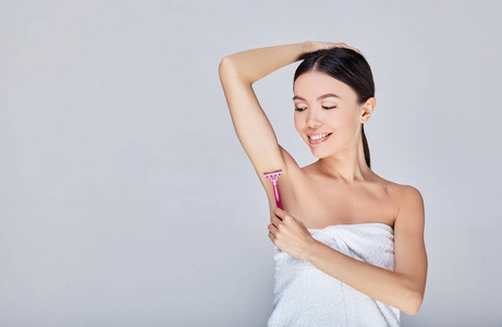 可爱的亚洲年轻女子在灰色背景上刮腋毛.照片