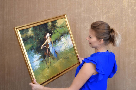 一个女人手里拿着一张照片。卡丽娜的油在房间的墙上。室内装饰风景画。