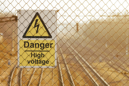 日落时，铁网围栏上的黄色高压警告标志。