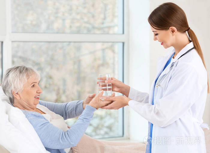女医生在门诊给患有帕金森综合征的老年妇女喝一杯水