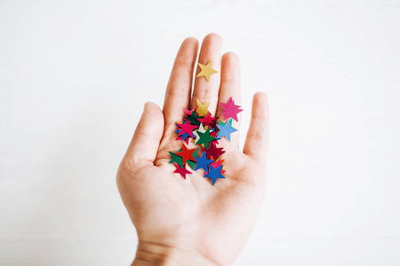 手拿五颜六色闪闪发光的星星装饰在白色的背上照片