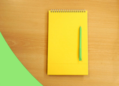 黄色空白写字板和一支绿色钢笔放在木制书桌上，平躺着