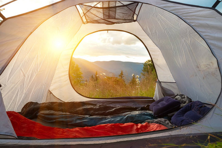 从旅游帐篷上可以看到山上草地上花丛里，清晨太阳升起的时候。旅游帐篷