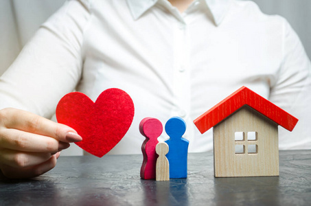 在一个微型家庭和家庭附近，一个女人手里拿着一颗红色的心。财产保险和房屋的概念。家庭安全。人寿和健康保险。保护和安全。代理人
