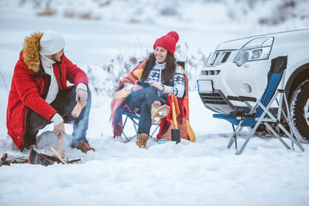 冬天，男人和女人坐在篝火旁的椅子上。汽车旅行。