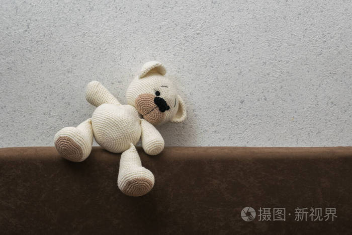 一只倒下的白色针织小熊躺在沙发上靠着一堵浅色的墙