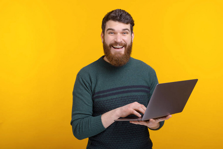 图为快乐的年轻人站在黄色背景上使用笔记本电脑