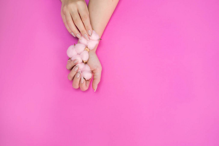 在明亮的背景上，用柔和的粉红色棉质，为美丽的女性修指甲。