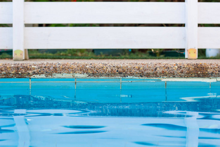 游泳池边柔和的焦点蓝色水面前景和白色木质甲板花园围栏背景度假酒店放松空间