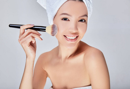 一个特写镜头，一个快乐的年轻亚洲女人用刷子在脸上擦粉。