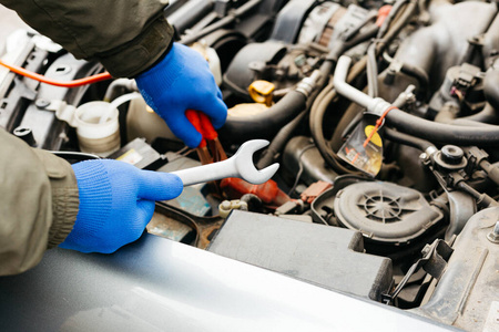 汽车机械工程师在修理汽车的过程中使用扳手。汽车修理工的男性手拿着扳手在车库里工作。在汽车修理站工作的戴手套的人。