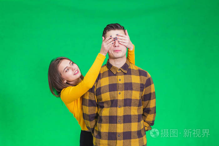 顽皮的女孩用手捂住男朋友的眼睛在绿色的背景上