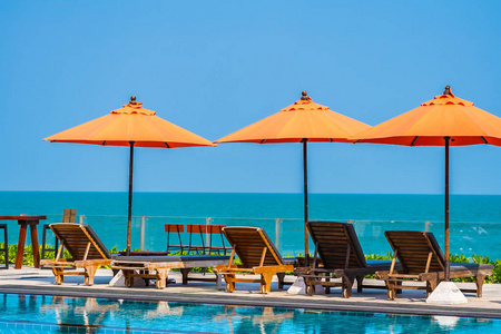 在炎热的海边的室外游泳池周围放着雨伞和椅子