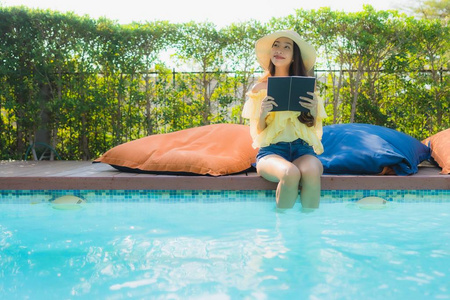 年轻的亚洲女人在户外游泳池边看书