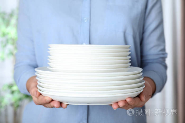 女人拿着一叠干净的盘子在模糊的背景上靠近