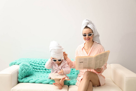 Mother and little daughter in bathrobes with newspapers sitting 