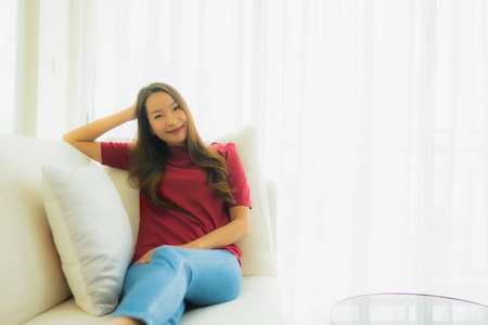 美丽的年轻亚洲女性坐在沙发上开心的微笑