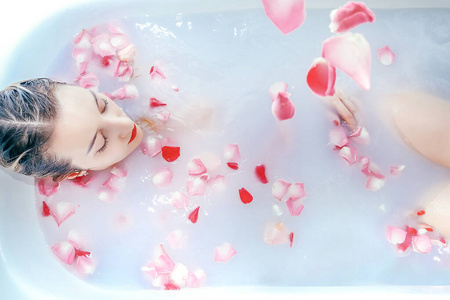 牛奶花瓣年轻性感的女孩正在用玫瑰花瓣洗牛奶浴照片
