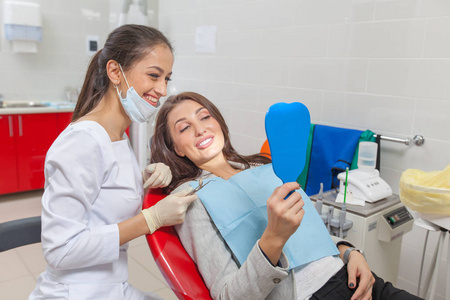 牙医。牙医办公室的一位女士对着镜子检查自己的牙齿，微笑着。