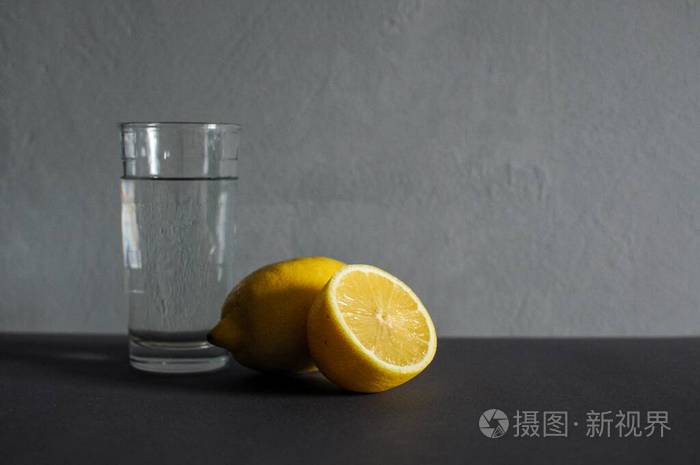 Glass of pure water with slice of lemon on dark grey background.