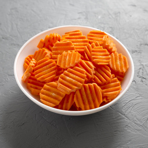 Fresh Raw Organic Carrot Chips in a bowl over gray surface, low 