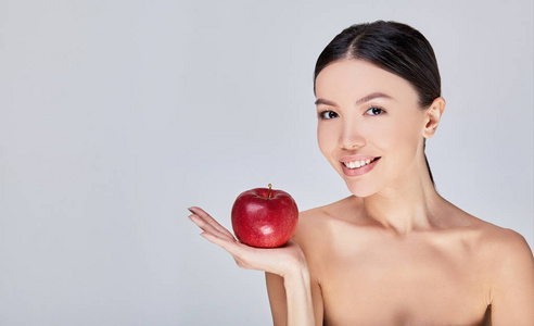 近距离看，一位皮肤完美的亚洲女性手掌中握着一个红苹果。