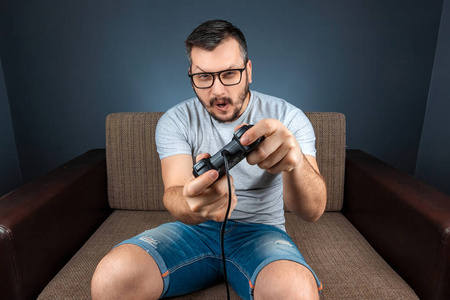 一个男人坐在沙发上玩电子游戏机。休息日，娱乐，休闲。