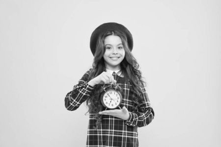 复古是永恒的。快乐的小孩拿着黄色背景的复古钟。小女孩微笑着用复古设计的时钟。可爱的孩子和复古风格的复古时钟