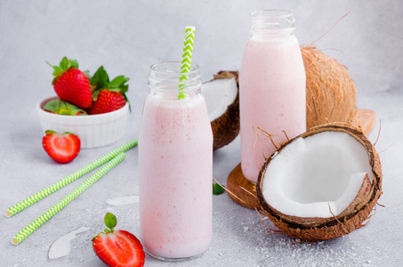 草莓椰子奶昔放在一个灰色背景上有吸管的玻璃罐里。健康食品理念。水平方向