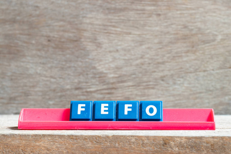 在红色架子上的木制背景上贴上单词FEFO先过期先出的字母