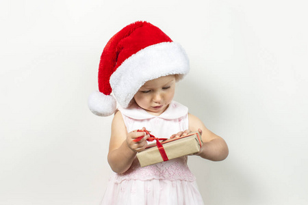 一个戴着圣诞老人帽子的小孩拿着一份礼物放在浅色的背景上。横幅。圣诞节和寒假礼物概念，家庭幸福
